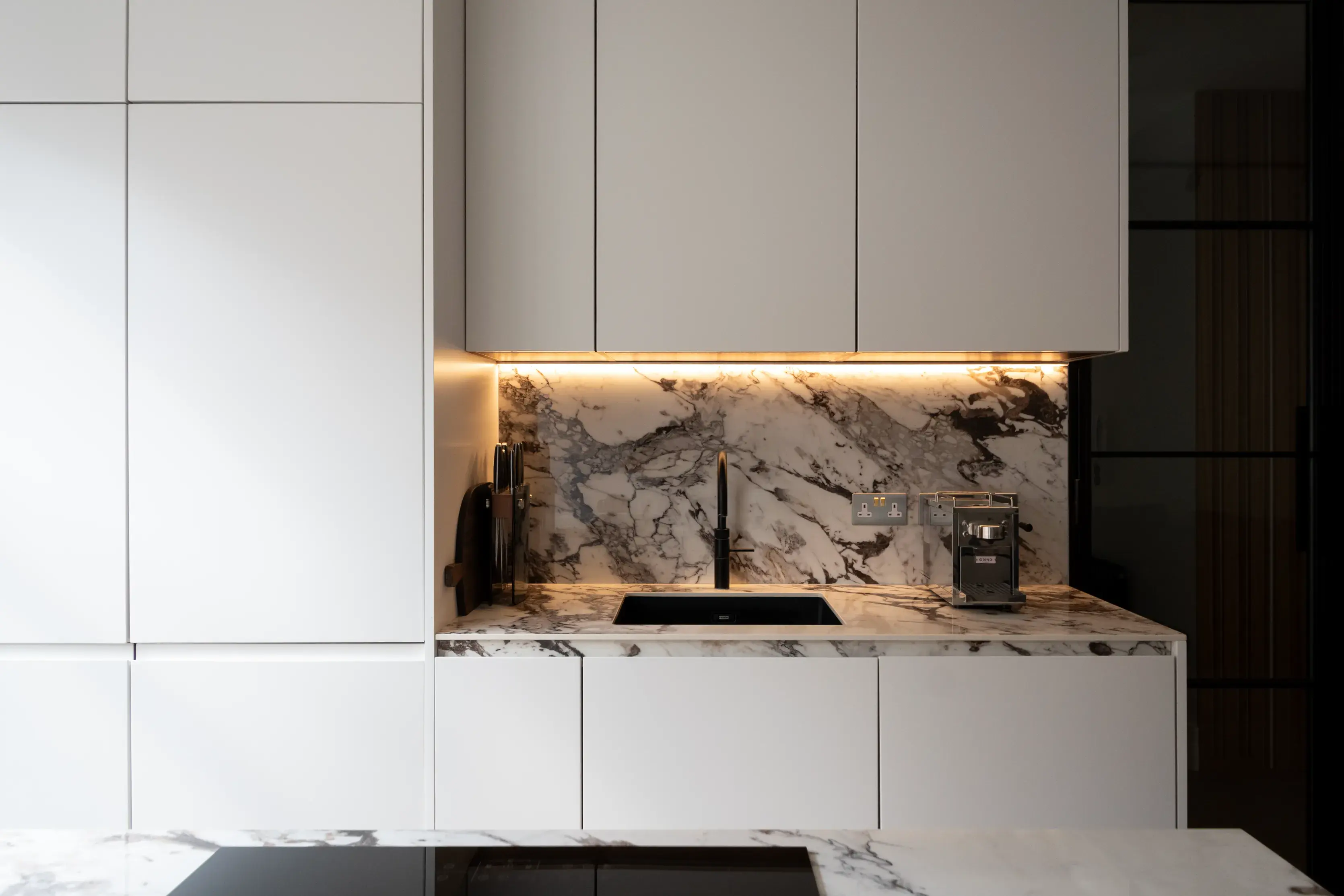 Handleless white kitchen units with under-cabinet lighting and marble splashback